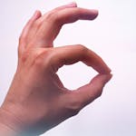 A close-up of a hand making an OK gesture, with a light background and soft lighting.