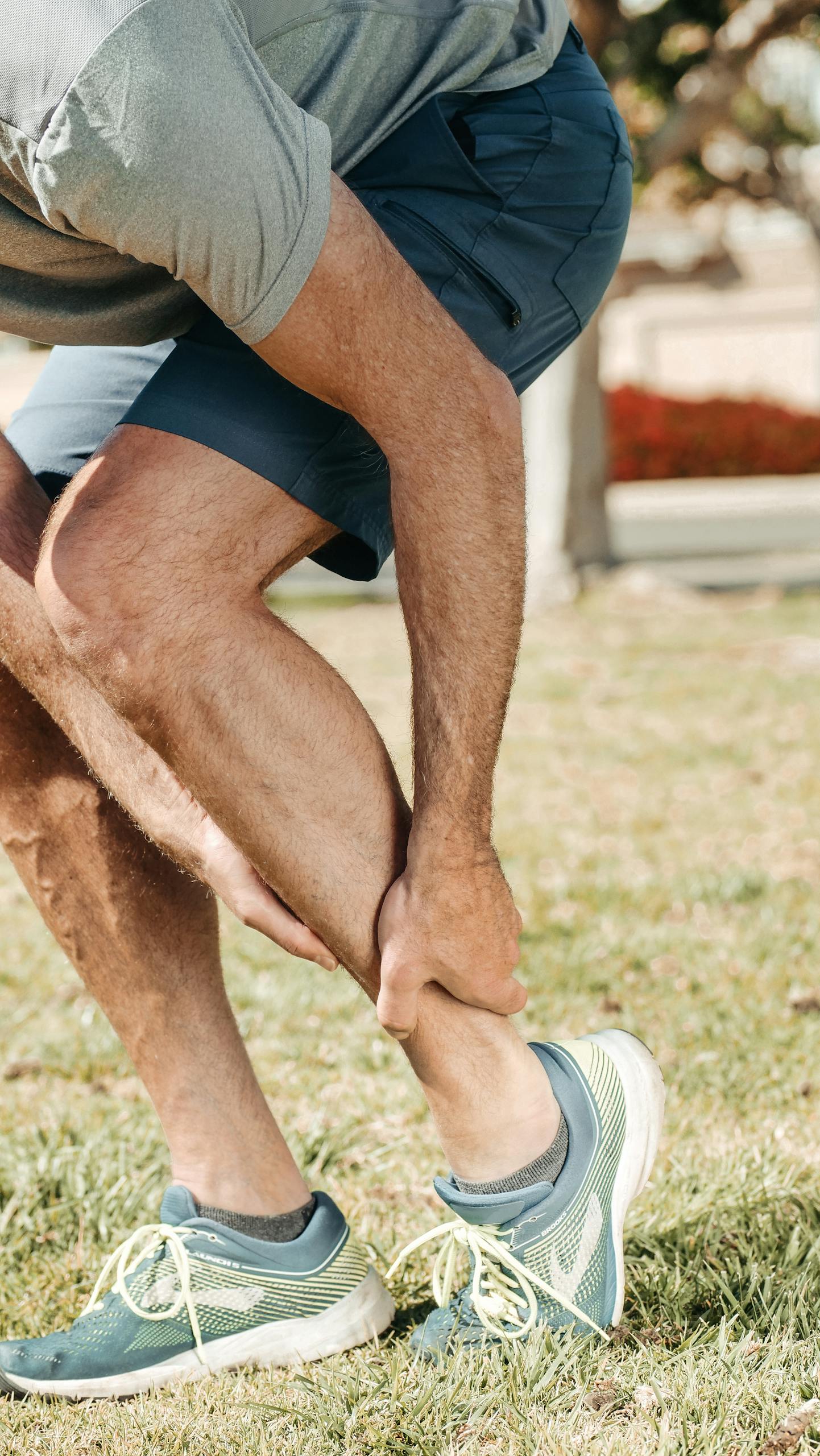 Adult male grabbing ankle due to injury in outdoor setting, wearing rubber running shoes.