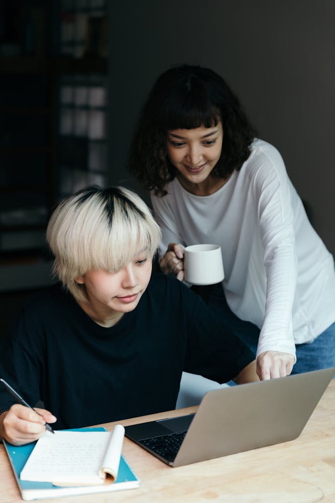 Two young women working together at home using a laptop, sharing ideas and planning.